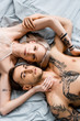 © LIGHTFIELD STUDIOS - Top view of tattooed couple looking at camera while touching each other on bed