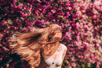 Wall Mural - Closeup portrait of a lovely girl in a park with blooming Japanese sakura trees. Romantic young blonde in a dress posing on a background of spring flowering trees. Cherry blossoms.