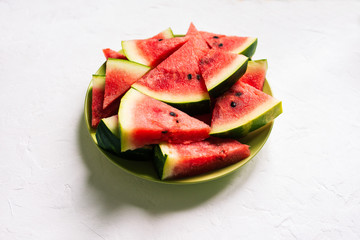 Fresh watermelon in a green plate on a white table. Slices of a watermelon in a triangular shape. Natural background with shadows.