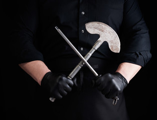 Wall Mural - male cook in black uniform and black latex gloves holds a large sharp vintage knife for meat and vegetables and a metal sharpener for knives