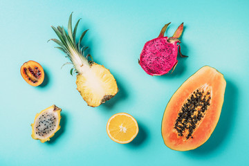 Creative layout made of exotic fruits - papaya, pineapple, dragon fruit, pitahaya, tamarillo fruit on blue background. Flat lay. Top view. Copy space. Summer food, tropical fruits concept. Vegan