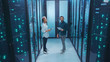 © Fractal Pictures - Couple of mixed-race technicians walking in database corridor of server room discussing work solving tech issues coworking in data center cyber security.