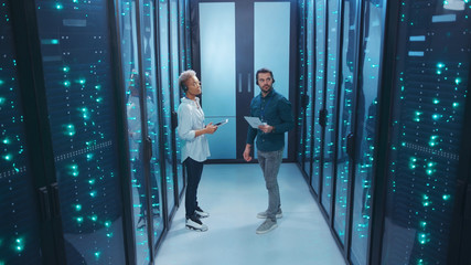 Wall Mural - couple of mixed-race technicians walking in database corridor of server room discussing work solving