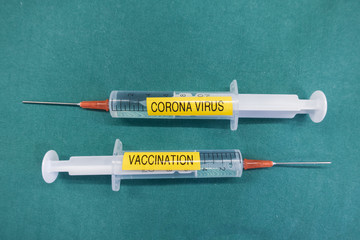 2 syringes labelled Corona Virus and vaccination are on a green cloth