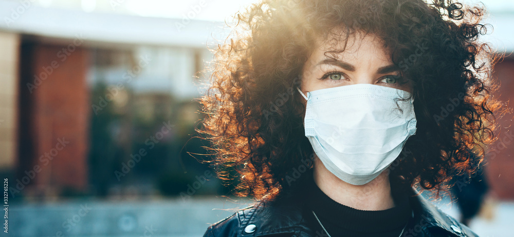 Close up portrait caucasian businesswoman with curly hair is looking at camera while wearing a protective mask - obrazy, fototapety, plakaty 