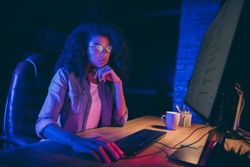 Wall Mural - Profile photo of workaholic dark skin programmer lady look screen monitor check debugging system errors work overtime wear specs casual shirt sit table chair night office indoors