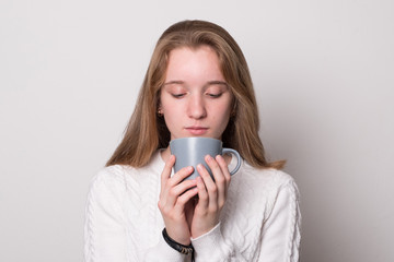 Wall Mural - Charming girl with a mug of tea. Cute teenager girl with blond hair holds a mug. Girl drinks from a mug.