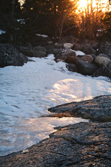 Wall Mural - Ice on a cliff with the sun and forest in the background