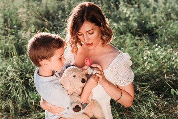 Cute blond boy giving rose to his beautiful mom. Outdoors. Mothers day