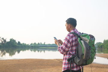 a backpack man standing on the river and see over view in nature.tourist use smart phone and enjoyin