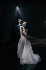 The bride and groom in wedding dresses and in black medical masks decorated with fresh flowers