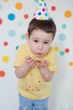 © aprilante - Toddler boy in the birthday hat on a background of wall with colorful circles