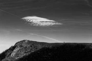 Two distant people on a mountain peak with a cloud above them