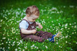 © Elena  - Charming boy among green grass and beautiful daisies on a summer day. A small child has fun in the fresh air. Baby explores the nature of