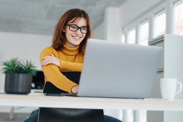 Wall Mural - Young businesswoman smiling as she works on laptop