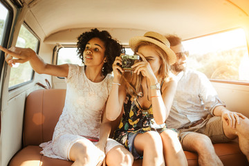 Three best friends travel in a minivan bus and explore new places. Two girls and one boy having good times. Taking pictures and selifies. Hugging and kissing eachother