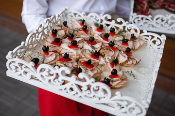 Wall Mural - Cropped images of waiter holds cold snacks on wooden stand with cold meats. Variety of tasty delicious snacks. Corporate birthday party event