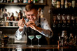 © fesenko - young smiling barman decorates two glasses with cocktails.