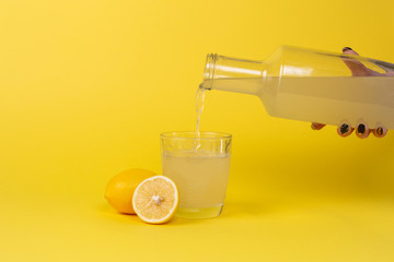 Lemon juice is poured into a glass with a glass bottle. Whole and cut lemons lie nearby.