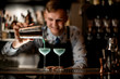 © fesenko - young smiling bartender pours cocktail from shaker into glasses