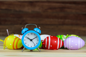 Wall Mural - Easter colored eggs and alarm clock on wooden background