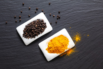 Wall Mural - Healthy food and alternative medicine ingredient concept organic Black peppers and turmeric powder in square ceramic cup on black slate stone board with copy space.