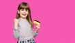 © Svetlana - Smiling Pretty child girl with hands up in winner pose holding credit card while rejoices over purple background
