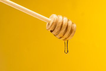 dripping sweet honey from wooden dipper on yellow background