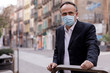 Manager con mascherina guarda serio verso lo sfondo in contesto urbano