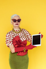 Wall Mural - Stylish senior woman holding digital tablet isolated on yellow