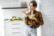© rh2010 - Portrait of a young and cheerful woman eating healthy salad on the kitchen at home. Healthy eating, wellbeing and lifestyle concept
