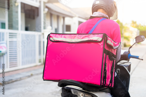 Motorbike delivery man wearing pink uniform and ready to send food.Delivering Food In City.Delivery man of takeaway with isothermal food pink case box driving find home.Express food delivery service.