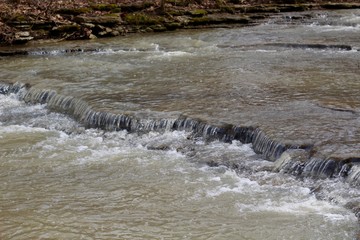 The small waterfall in the flowing water of the creek.