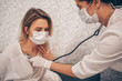 © Алина Троева - Doctor nurse in protective face mask listening to breath with a stethoscope suspecting Coronavirus (COVID-19). First symptoms concept. Woman sick of flu viral infection in home isolation quarantine