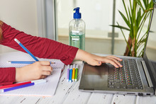 Distance Learning Online Education. Schoolgirl Studying At Home With A Laptop And Doing School Homework. Training Books And Colored Felt-tip Pens On The Table, Gel With Alcohol 70 Percent