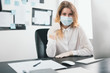 © studioprodakshn - young blond woman manager in medical protection mask and gloves works in office during Covid-19 epidemy, shows like sign, virology concept