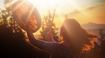 beautiful shamanic girl playing on shaman frame drum in the nature.