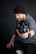 © KseniyaK - young adult man with a beard in a black hat holds a black skull in his hands