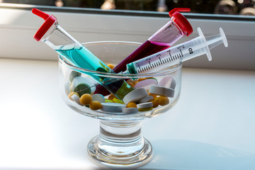 yellow, white, green tablets and two test tubes with red and blue liquid in a transparent glass vase