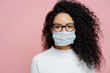 © VK Studio - Covid-19, infectious virus. Close up shot of young woman with curly bushy hair, wears transparent glasses and medical disposable mask, cares about her health, protects in dangerious situation