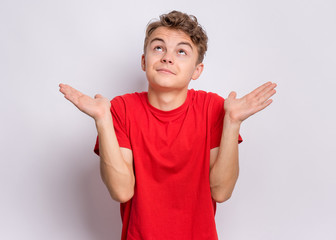 Poster - Teen boy showing helpless gesture with hands - I do not know. Cute young teenager in red t-shirt, on grey background. Shrugging, confused child making helpless sign and looking up.