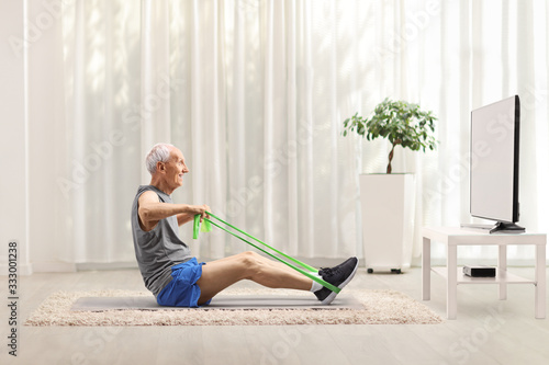 Fotografía Senior man exercising with an elastic band in front of a tv at home