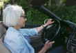 © Rob and Julia Campbell/Stocksy - Relaxed older woman driving convertable car.