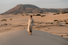 Woman In Beige Trench Coat Walking In Desert.