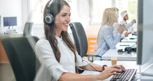 Portrait Of Beautiful Smiling Business Woman With Headset Using Computer In Office