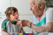 © Cavan Images - Grandmother feeding granddaughter in the kitchen