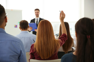 Wall Mural - Young woman raising hand to ask question at business training indoors, back view