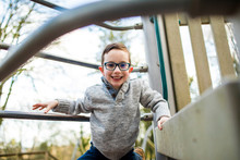 Portrait Of Young Boy Climbing On Playground Equipment.