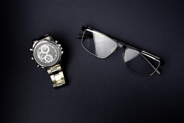 Eyeglasses and mens wrist watch on black background