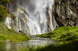 Waterfall cascading over rocks in a lush green grassy nature landscape
